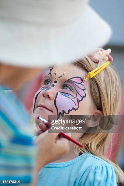 blond girl getting a butterfly painted on her face - kinder schminken stockfoto's en -beelden