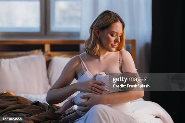 happy beautiful blonde woman looking away while breastfeeding her adorable newborn child - breastfeeding stock pictures, royalty-free photos & images