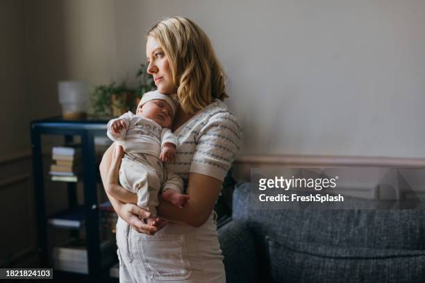 serious beautiful blonde woman looking away while taking care of her adorable newborn child - beautiful blonde babes stockfoto's en -beelden