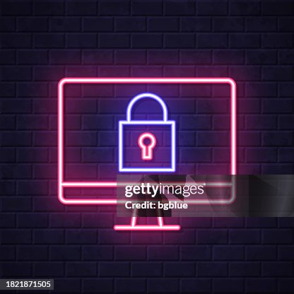 Desktop computer with padlock. Glowing neon icon on brick wall background Desktop computer with padlock. Glowing neon icon on brick wall background
