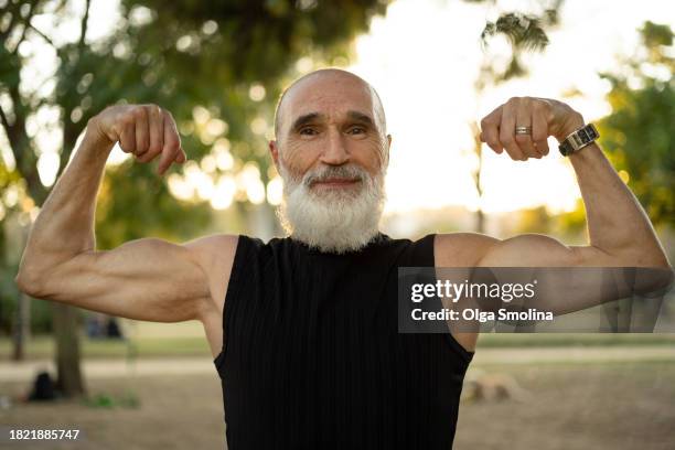 senior bearded man standing in park.active healthy lifestyle,wellbeing, doing sport outdoors - flexionar los músculos fotografías e imágenes de stock
