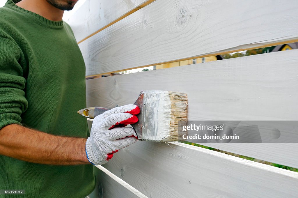 Hombre está pintando con cepillo valla de madera de color blanco