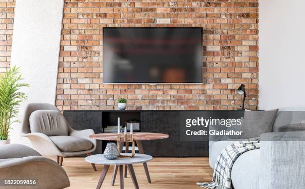 modern living room with a tv mounted on the brick wall, gray sofa, chairs and coffee table, and decoration - lcd television stockfoto's en -beelden