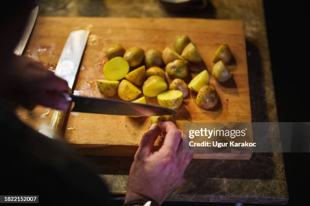 mann schneidet kartoffeln auf schneidebrett mit messer, kocht abendessen - kartoffel-wurzelgemüse stock-fotos und bilder