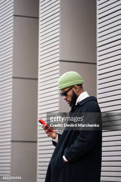 businesslike black man in long fashionable expensive overcoat messaging, reading in mobile phone - georgian man stock pictures, royalty-free photos & images