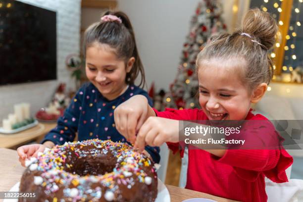 adorable caucasian sisters decorating the chocolate bundt cake together with sprinkles - bundtkaka bildbanksfoton och bilder