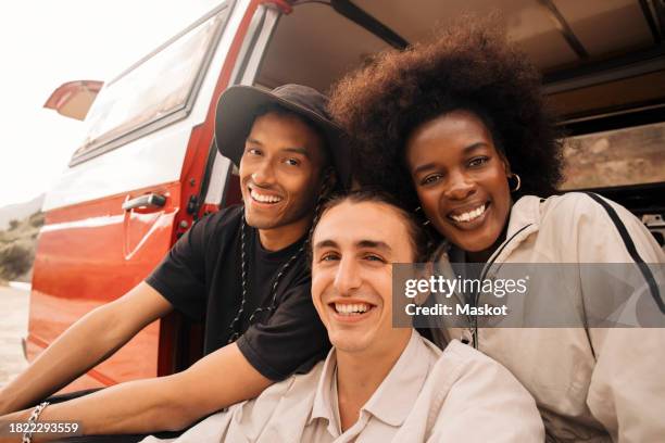 portrait of smiling young man sitting with male and female friends in van - 3 guy friends road trip stock-fotos und bilder