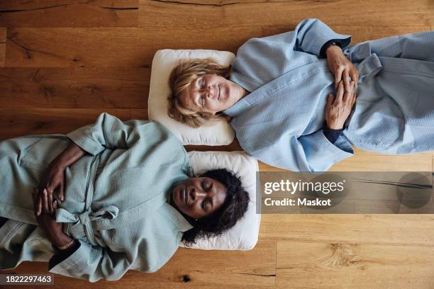 multiracial female friends wearing bathrobes while relaxing together on floor at home - cushion top view stock pictures, royalty-free photos & images