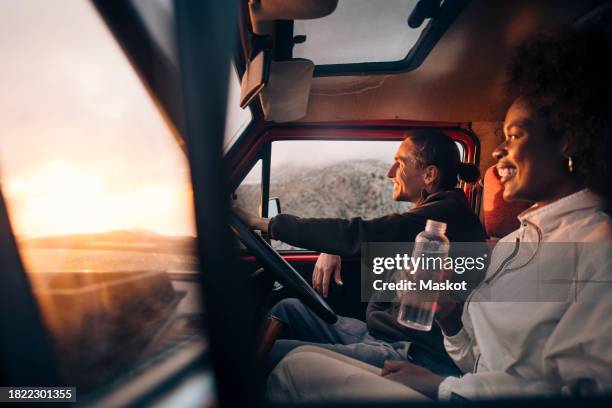 happy woman holding water bottle while sitting with male friend driving van on vacation - van life stock pictures, royalty-free photos & images