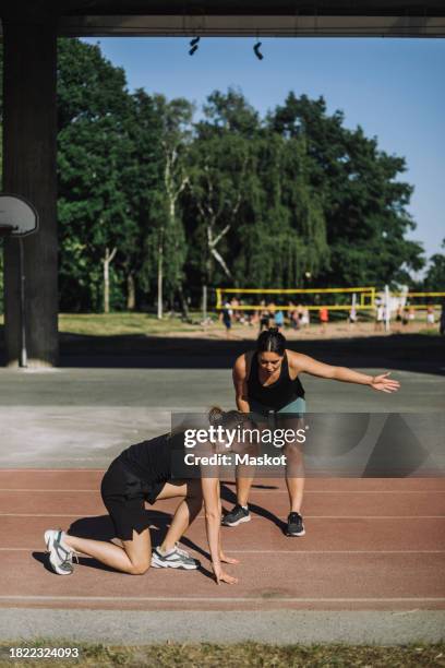 female coach assisting woman kneeling on running track - running coach stock pictures, royalty-free photos & images