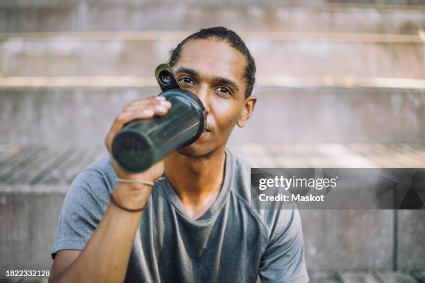 portrait of man drinking protein from shaker while sitting on steps - protein shaker stock pictures, royalty-free photos & images
