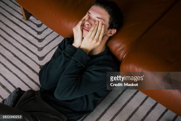 high angle view of man rubbing eyes while reclining on sofa at home - man headache bildbanksfoton och bilder