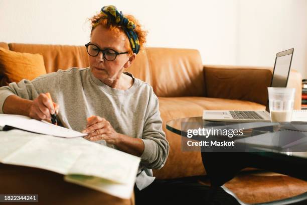 senior woman planning trip while sitting in living room at home - book icon stock pictures, royalty-free photos & images