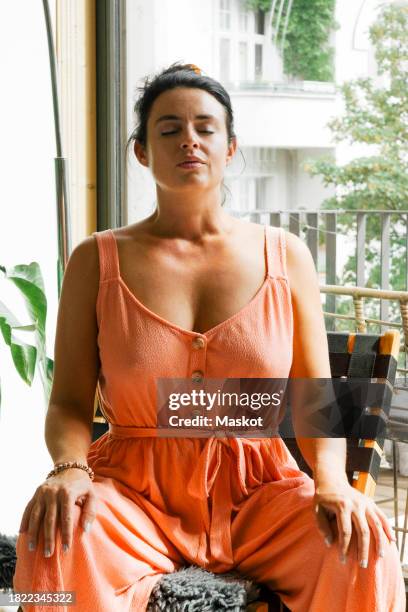 woman practicing breathing exercise while sitting on chair at home - hand on knee stock pictures, royalty-free photos & images