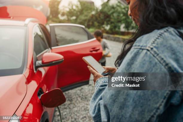 woman using smart phone next to electric car - next to stock pictures, royalty-free photos & images