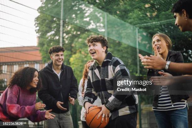 happy friends cheering teenage boy preparing to take shot while playing basketball at court - encouragement stock pictures, royalty-free photos & images