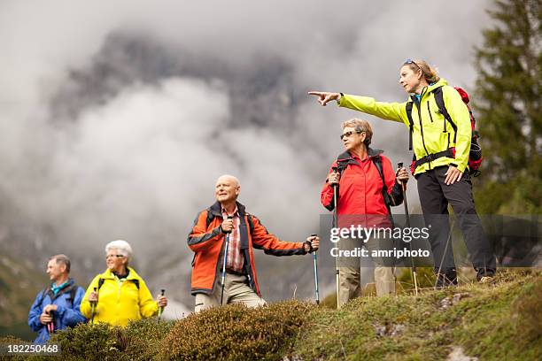 young female hiking guide showing senior group surrounding mount - tour guide stock pictures, royalty-free photos & images