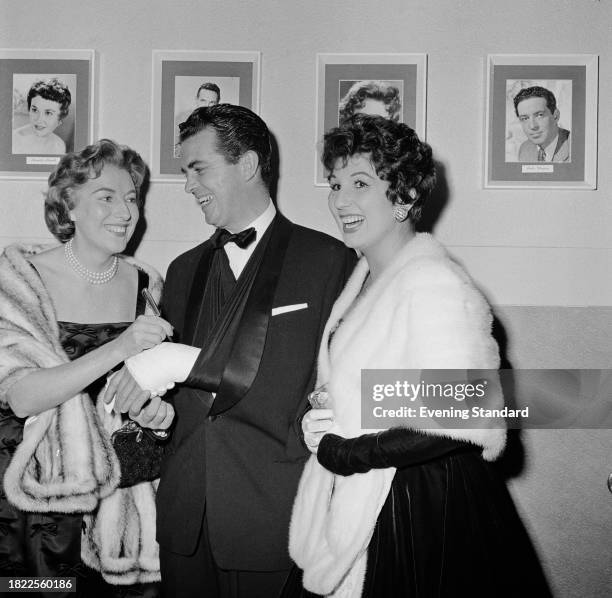 Actress and singer Vera Lynn signs the plaster cast on radio presenter Jimmy Henney's hand while pop singer Alma Cogan stands beside them, October...