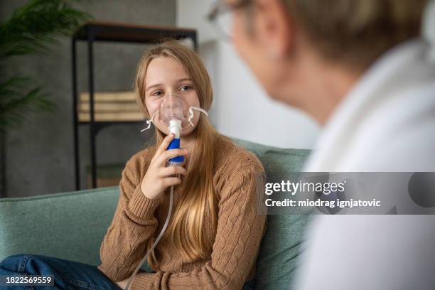 girl using a medical inhaler at home with her mother - nebulizer stock pictures, royalty-free photos & images