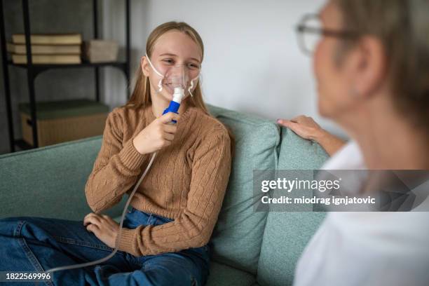 girl using a medical inhaler at home with her mother - nebulizer stock pictures, royalty-free photos & images