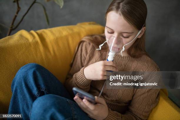 girl using her phone while using a nebulizer at home - nebulizer stock pictures, royalty-free photos & images