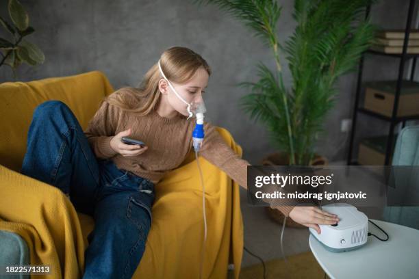 girl using her phone while using a nebulizer at home - nebulizer stock pictures, royalty-free photos & images