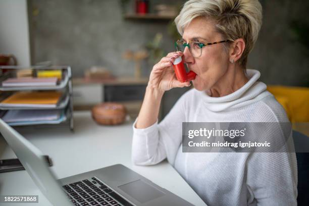 mulher com asma usando inalador enquanto trabalha em casa - inalador-de-alívio-para-asma - fotografias e filmes do acervo