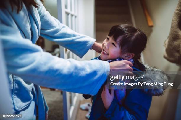 mom helping her daughter to put on a scarf in doorway at home before sending her to school in the morning - winter coat stock pictures, royalty-free photos & images