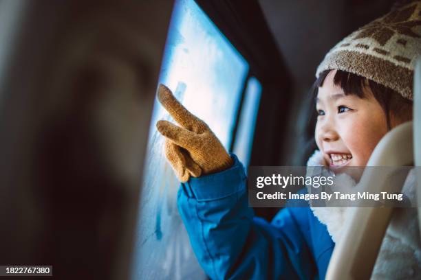 lovey cheerful girl in beanie hat & gloves drawing on condensed car window with finger while travelling in car - auto mieten stock pictures, royalty-free photos & images