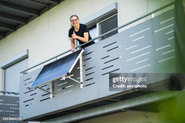 frau glücklich nach installation eines solarpanels auf dem balkon - balcony stock-fotos und bilder