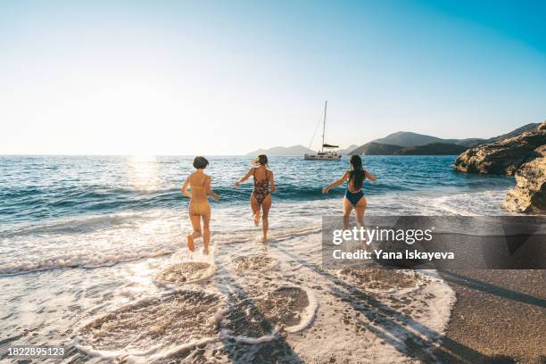 three friends having fun on the seaside in the salty sea waves, splashing water at each other - sailing ship stock pictures, royalty-free photos & images