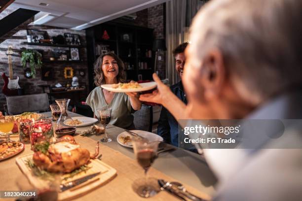 mature woman serving the dish to her father at christmas dinner - serving dish stock pictures, royalty-free photos & images