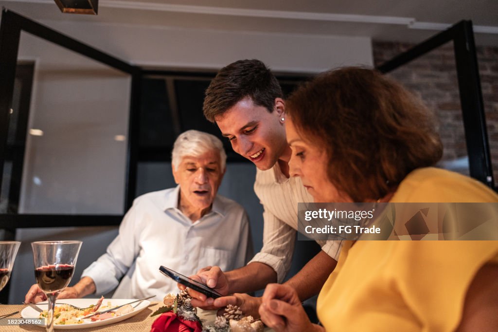Grandchild showing something on the mobile phone to his grandparents at Christmas dinner