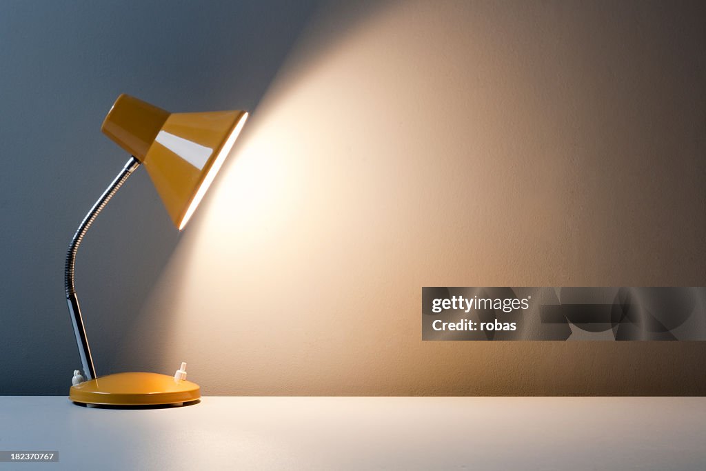 Profile of yellow desk lamp, turned on on white table