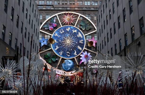 People walk through Rockefeller Center Plaza in front of the Christmas decorations on the facade of the Saks Fifth Avenue store on Fifth Avenue on...