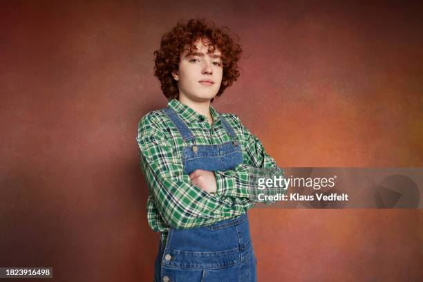 portrait of redhead teenage boy with arms crossed standing against brown background - blue checked pattern stock pictures, royalty-free photos & images