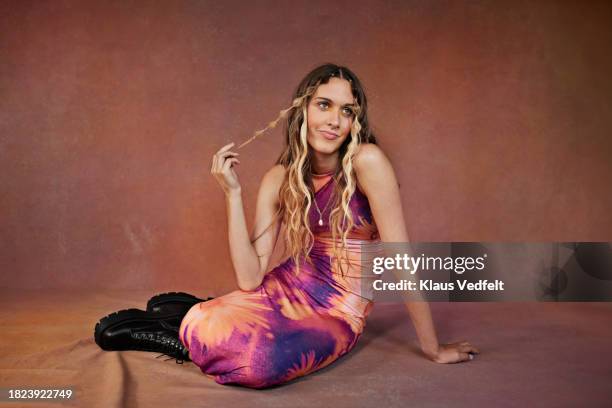 contemplative teenage girl holding hair while sitting against brown backdrop - hands on head stock pictures, royalty-free photos & images