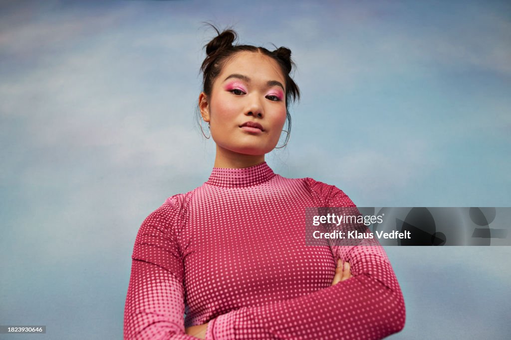 Portrait of confident teenage girl with arms crossed against colored background