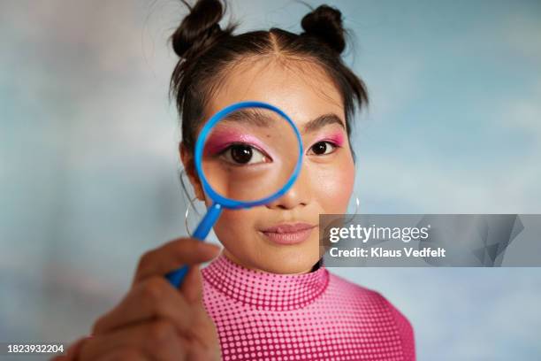portrait of teenage girl looking through magnifying glass against colored background - cor do olho humano imagens e fotografias de stock