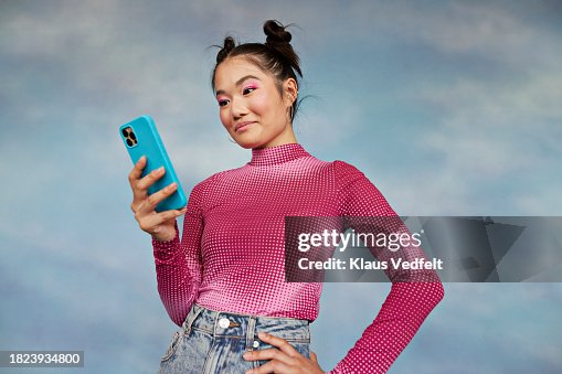 Teenage girl using mobile phone while standing against colored background