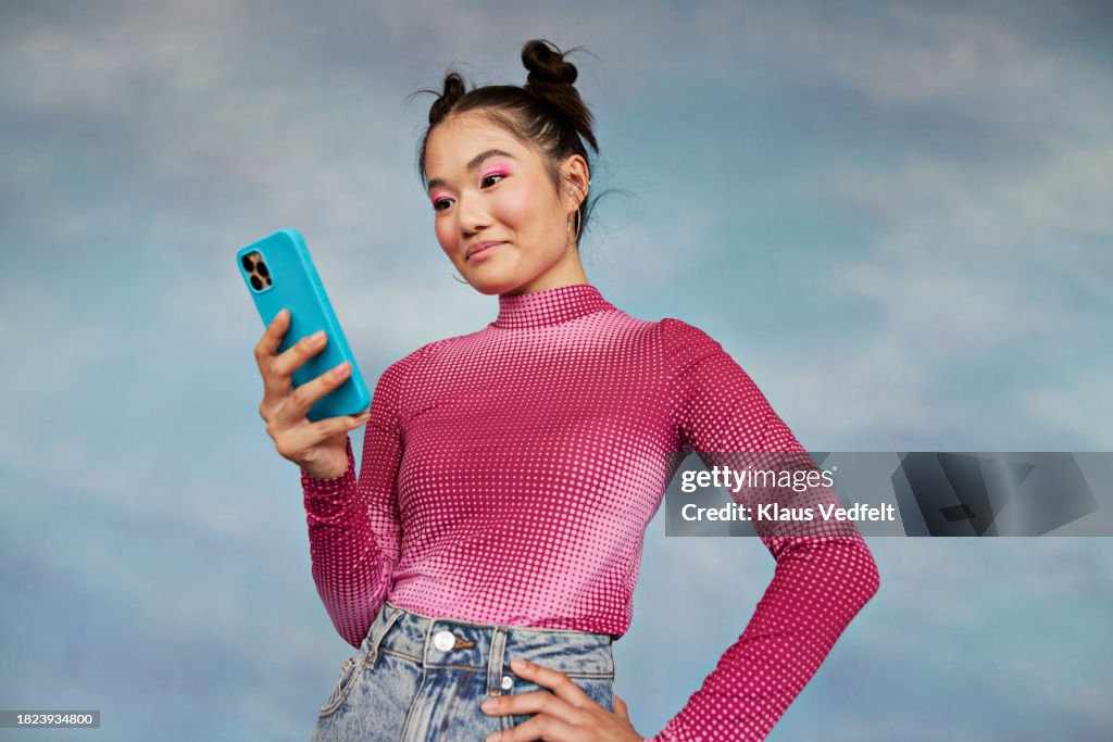 Teenage girl using mobile phone while standing against colored background
