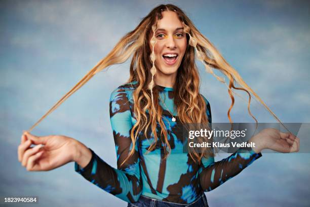 portrait of happy transgender girl holding hair while standing against colored background - highlights hair stock pictures, royalty-free photos & images