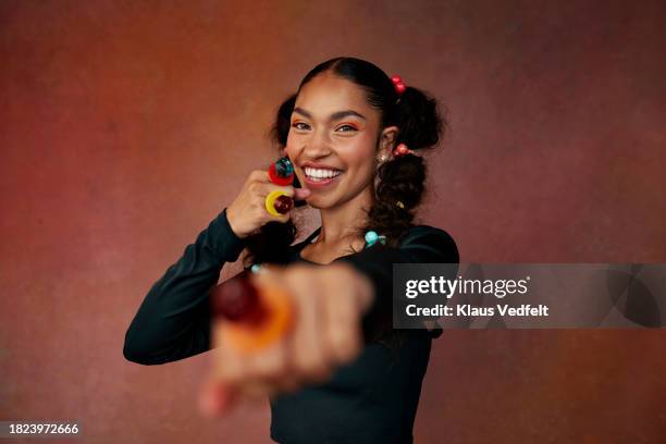 portrait of smiling teenage girl showing fists while standing against brown background - pigtail lollipop stock pictures, royalty-free photos & images