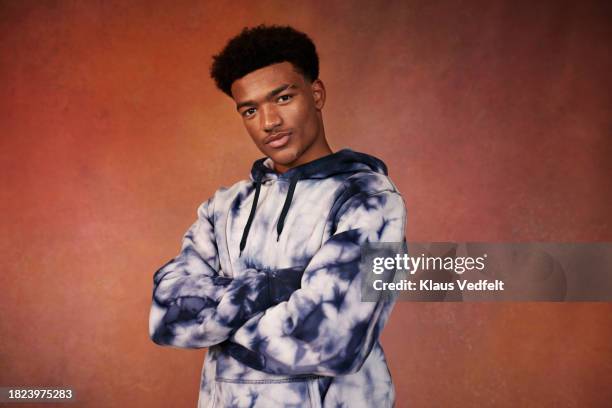 portrait of teenage boy in tie dye hooded shirt with arms crossed against brown background - one teenage boy only stock pictures, royalty-free photos & images