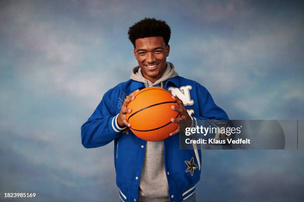 portrait of smiling teenage boy holding basketball standing against colored background - one teenage boy only stock pictures, royalty-free photos & images