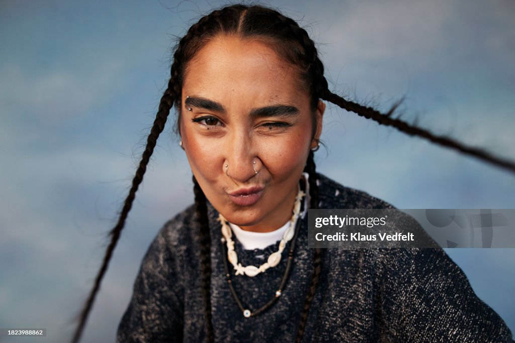 Portrait of non-binary person with braided hair puckering against colored background
