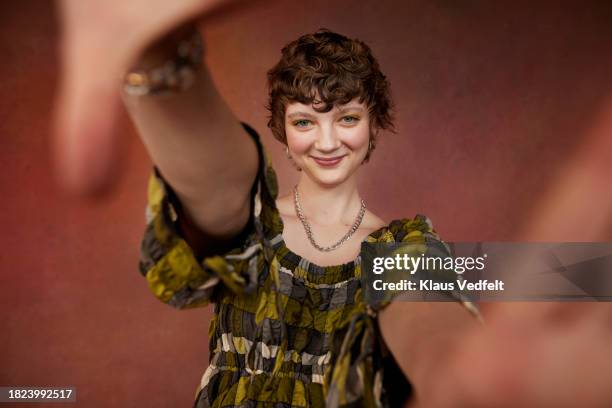 portrait of smiling teenage girl taking selfie while standing against brown background - kort haar stockfoto's en -beelden