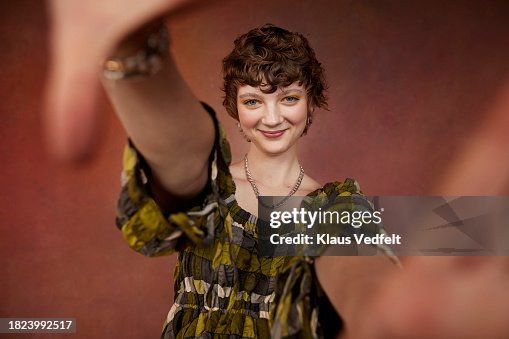 Portrait of smiling teenage girl taking selfie while standing against brown background Portrait of smiling teenage girl taking selfie while standing against brown background