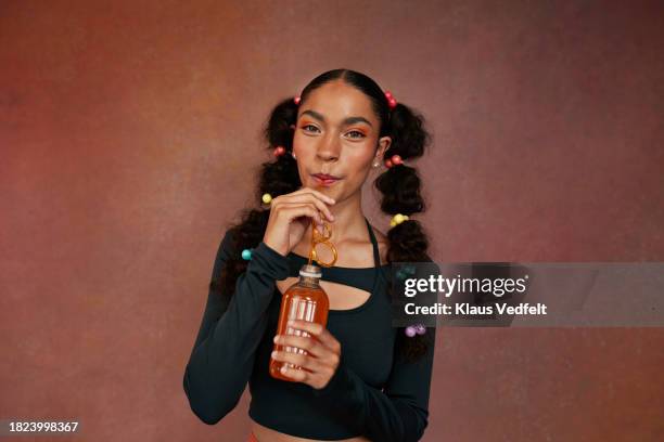 portrait of teenage girl drinking orange juice standing against brown background - accessoires stock-fotos und bilder