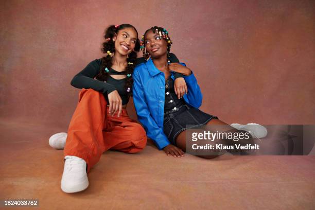 smiling teenage girl sitting arm around with female friend against brown backdrop - beautiful girls pic stock pictures, royalty-free photos & images